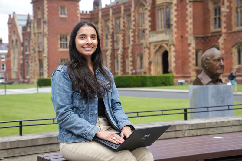 international female student sitting on laptop outside Queen's University Belfast